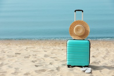 Photo of Turquoise suitcase, flip flops and straw hat on sandy beach, space for text