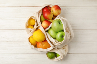Photo of Cotton eco bags with fruits on white wooden background, flat lay