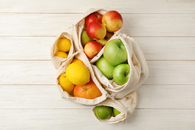 Cotton eco bags with fruits on white wooden background, flat lay