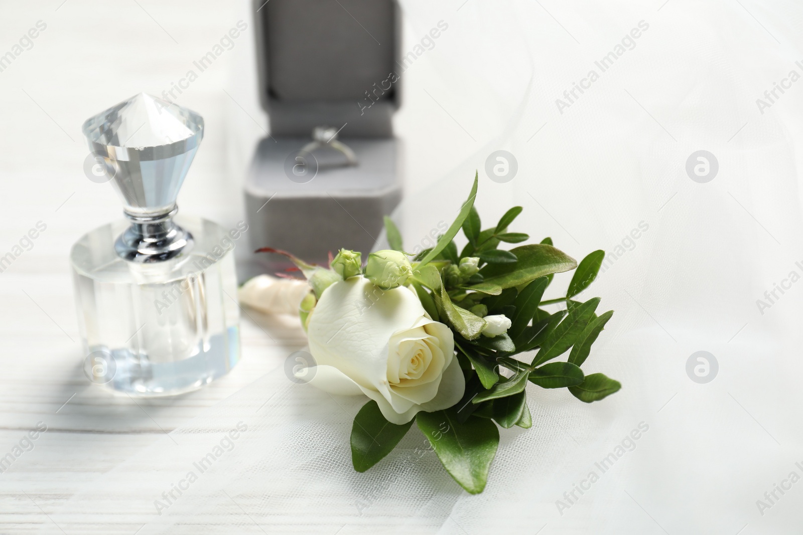 Photo of Wedding stuff. Stylish boutonniere, perfume and ring on white wooden table, closeup