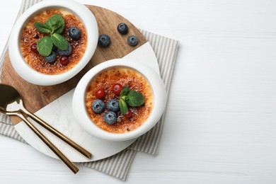 Photo of Delicious creme brulee with berries and mint in bowls on white wooden table, top view. Space for text
