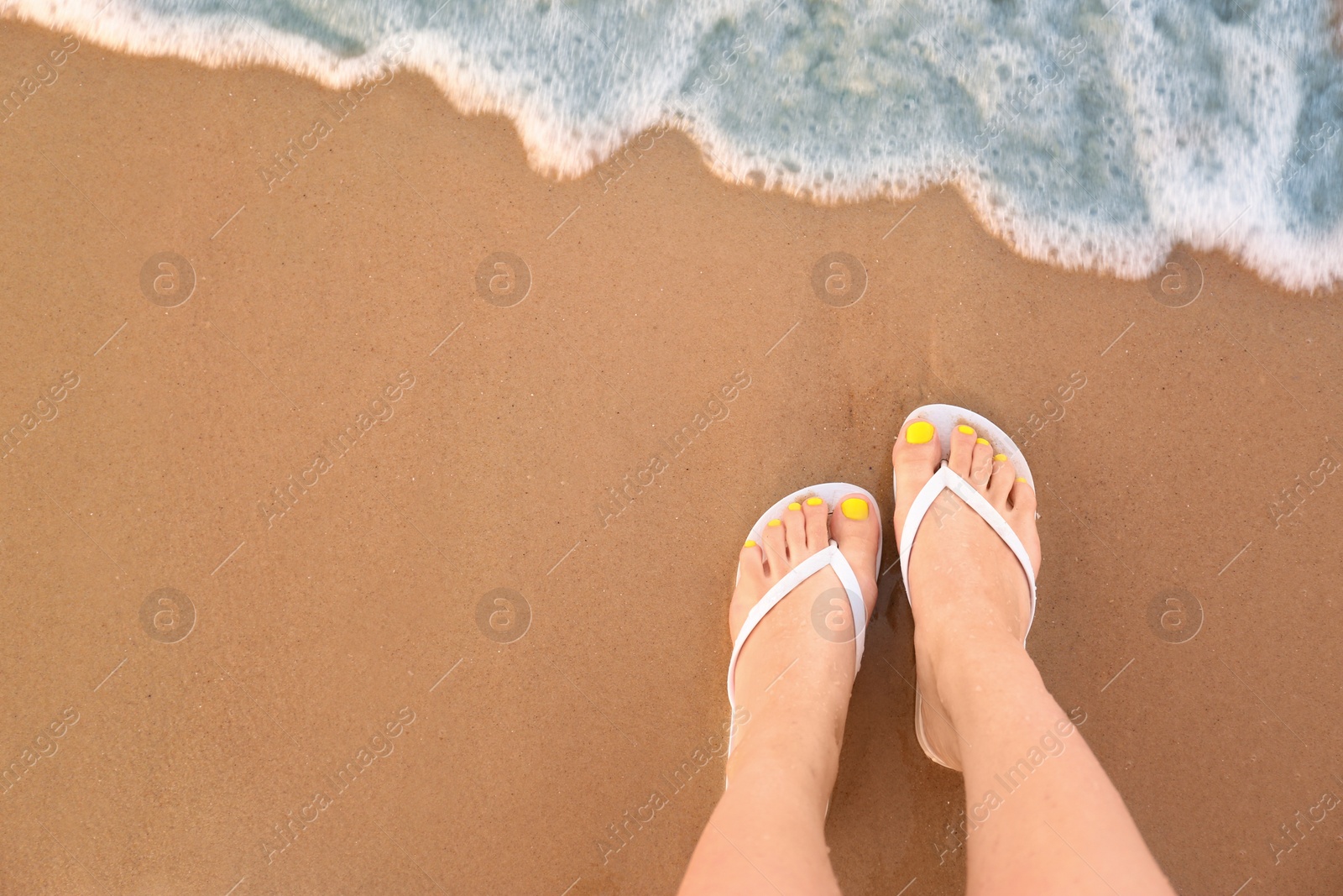 Photo of Top view of woman with white flip flops on sand near sea, space for text. Beach accessories