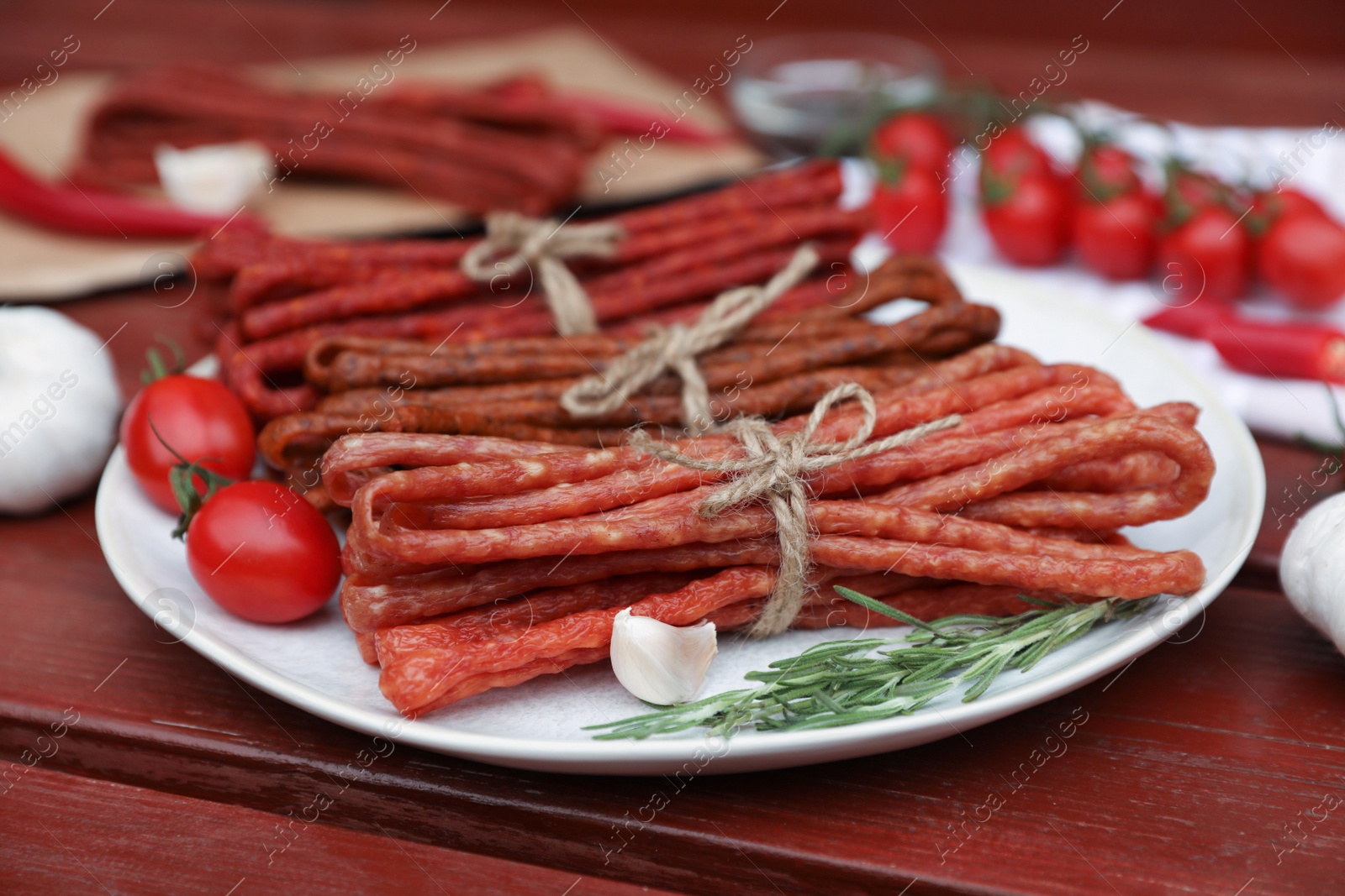 Photo of Bundles of delicious kabanosy with rosemary, garlic and tomatoes on wooden table