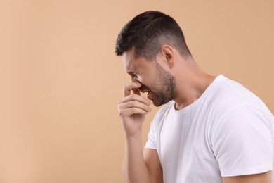 Allergy symptom. Man sneezing on light brown background. Space for text