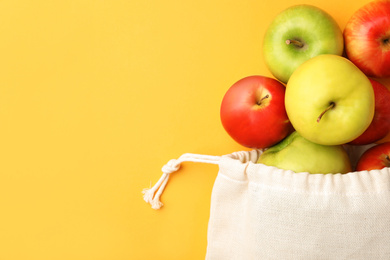Photo of Cotton eco bag and apples on yellow background, flat lay. Space for text