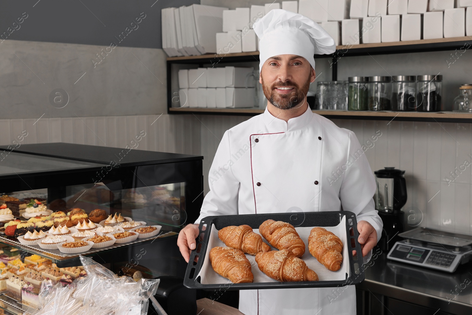 Photo of Professional baker with freshly baked croissants in store