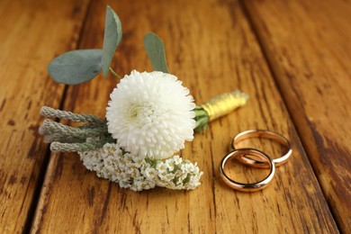 Small stylish boutonniere and rings on wooden table, closeup