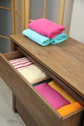 Wooden chest of drawers with different folded clothes indoors