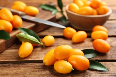 Photo of Fresh ripe kumquats and leaves on wooden table