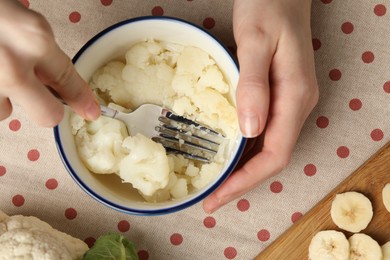 Photo of Woman making baby food with cauliflower at table, top view
