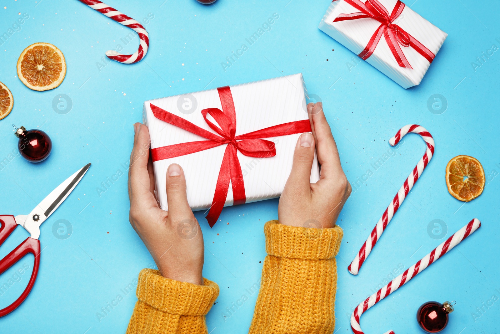 Photo of Young woman holding Christmas gift on light blue background, flat lay