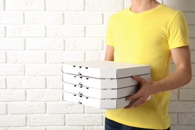 Photo of Courier holding pizza boxes near white brick wall, closeup with space for text. Food delivery service