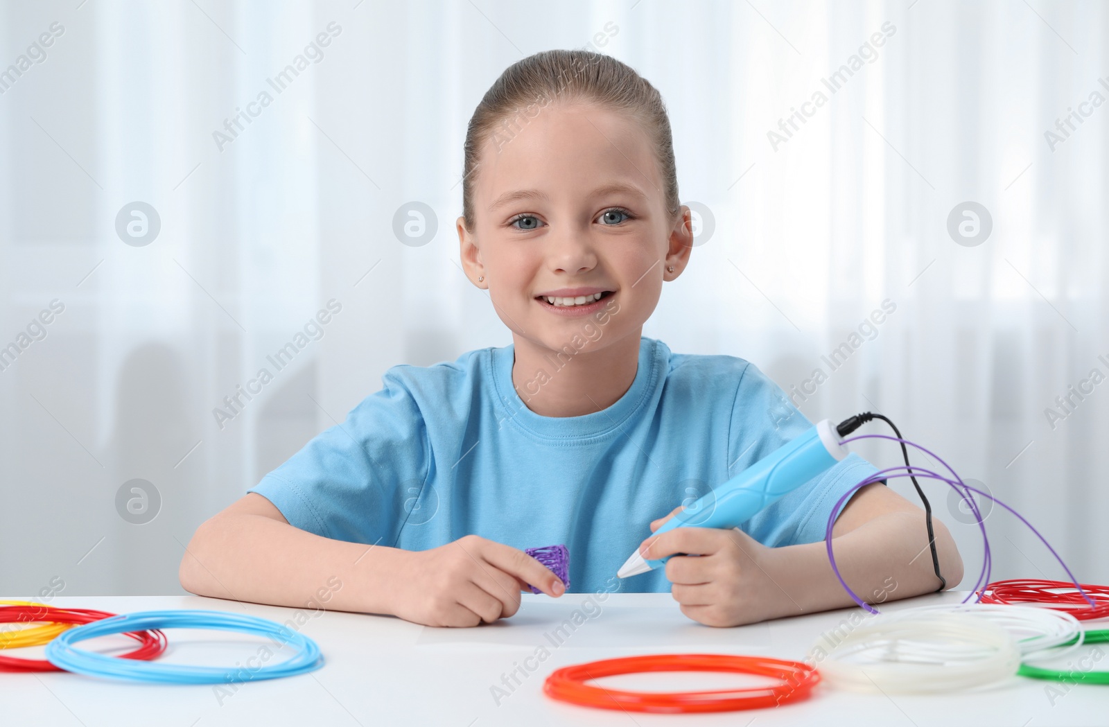 Photo of Girl drawing with stylish 3D pen at white table indoors