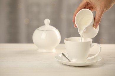 Woman pouring milk into cup at table indoors, closeup