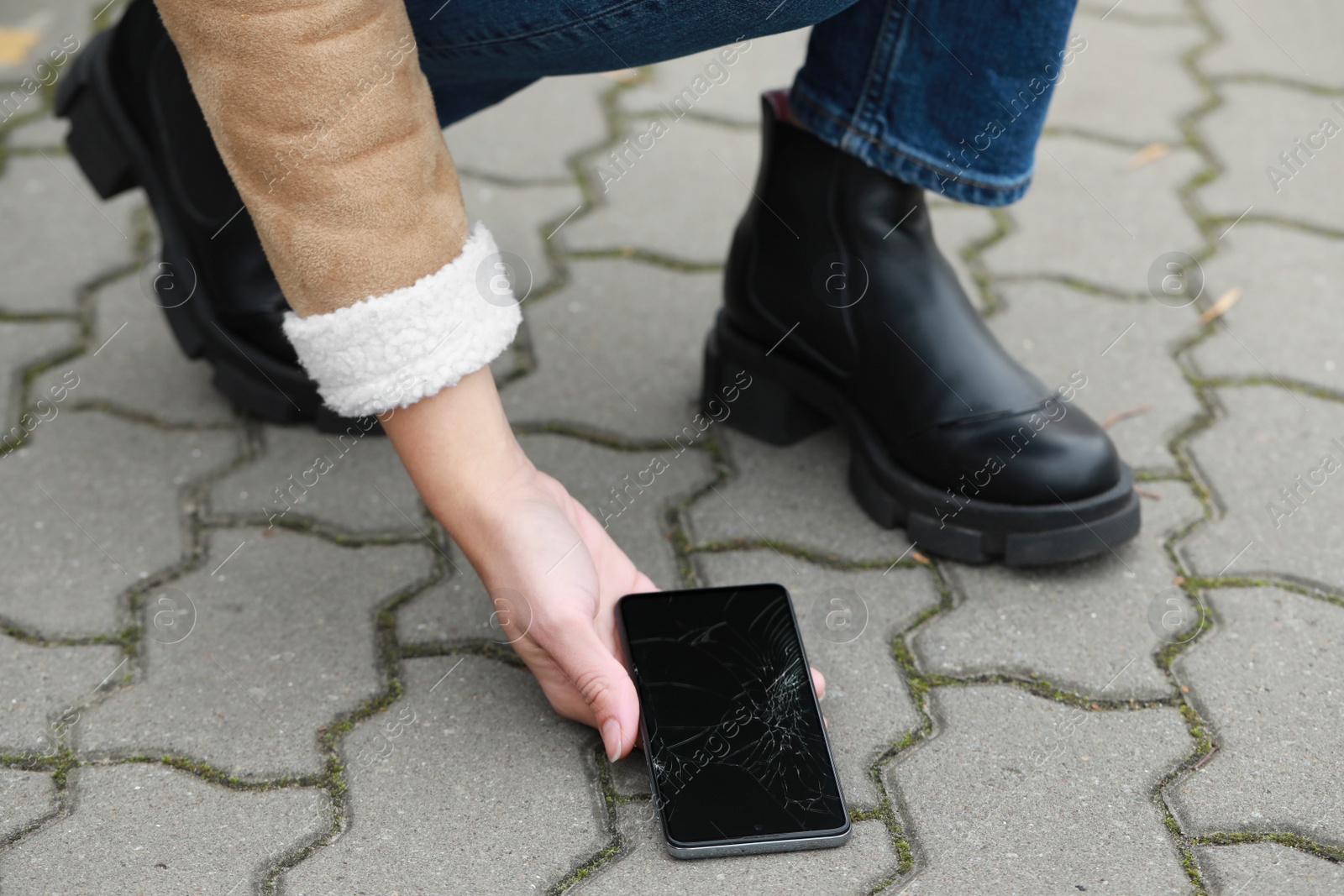 Photo of Woman taking dropped smartphone from pavement, closeup. Device repairing