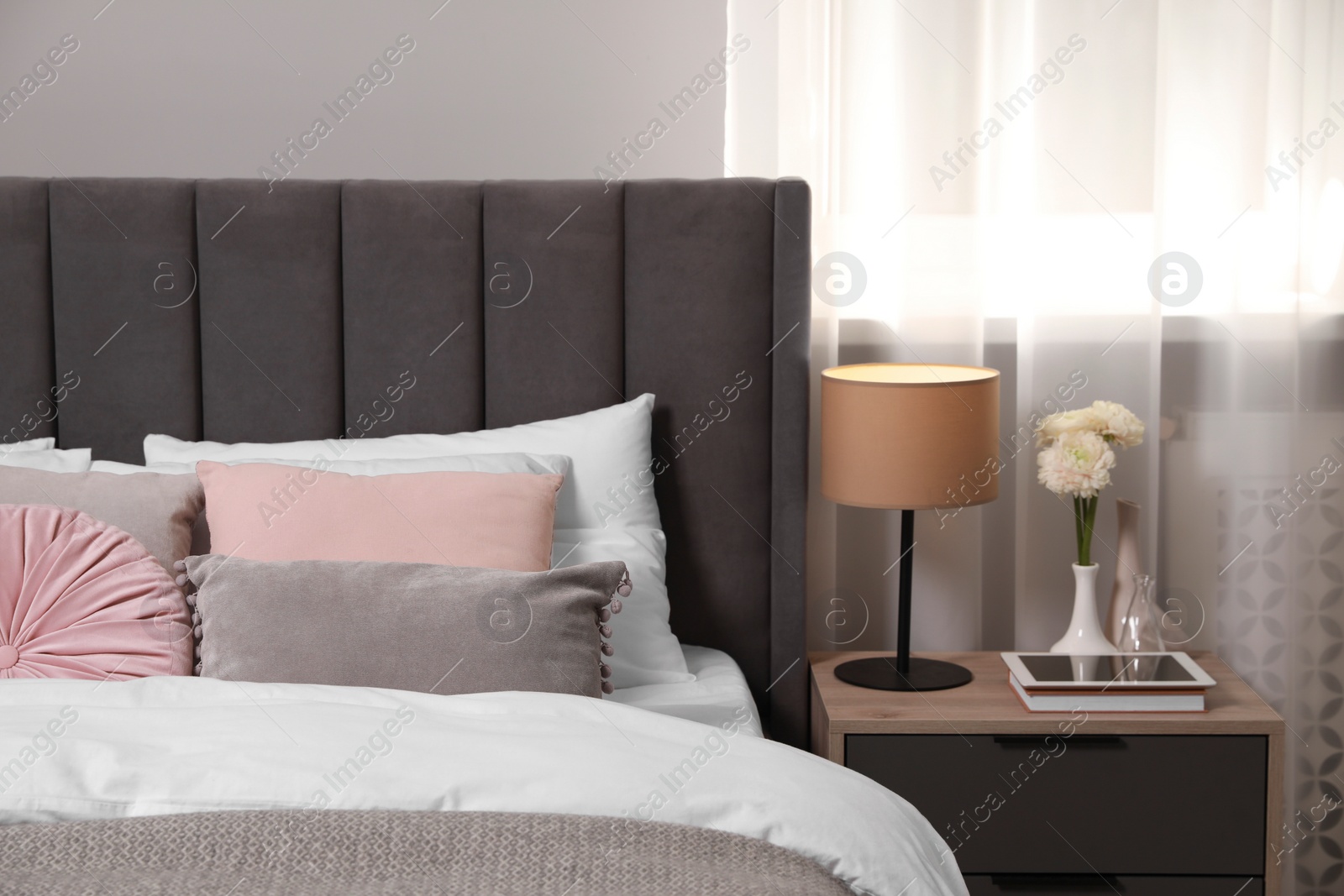 Photo of Comfortable bed with cushions, lamp and different decor on bedside table in room. Stylish interior