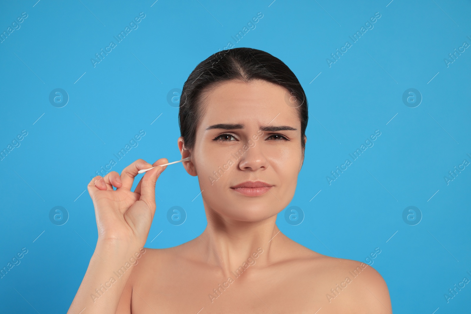 Photo of Young woman cleaning ear with cotton swab on light blue background