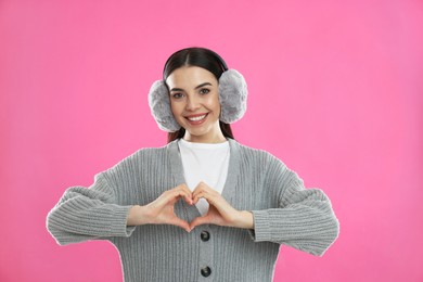 Photo of Beautiful young woman wearing earmuffs on pink background