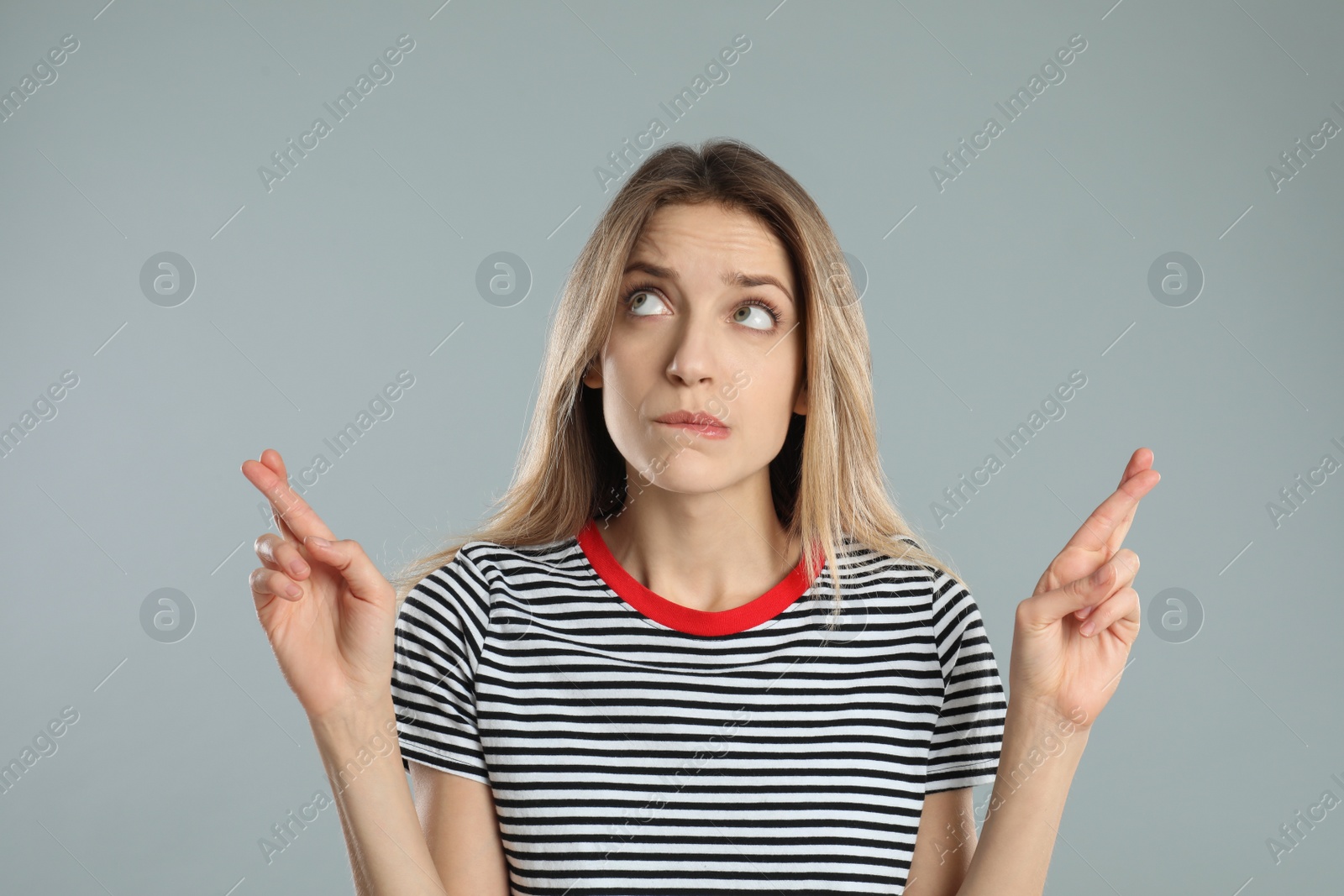 Photo of Woman with crossed fingers on light grey background. Superstition concept