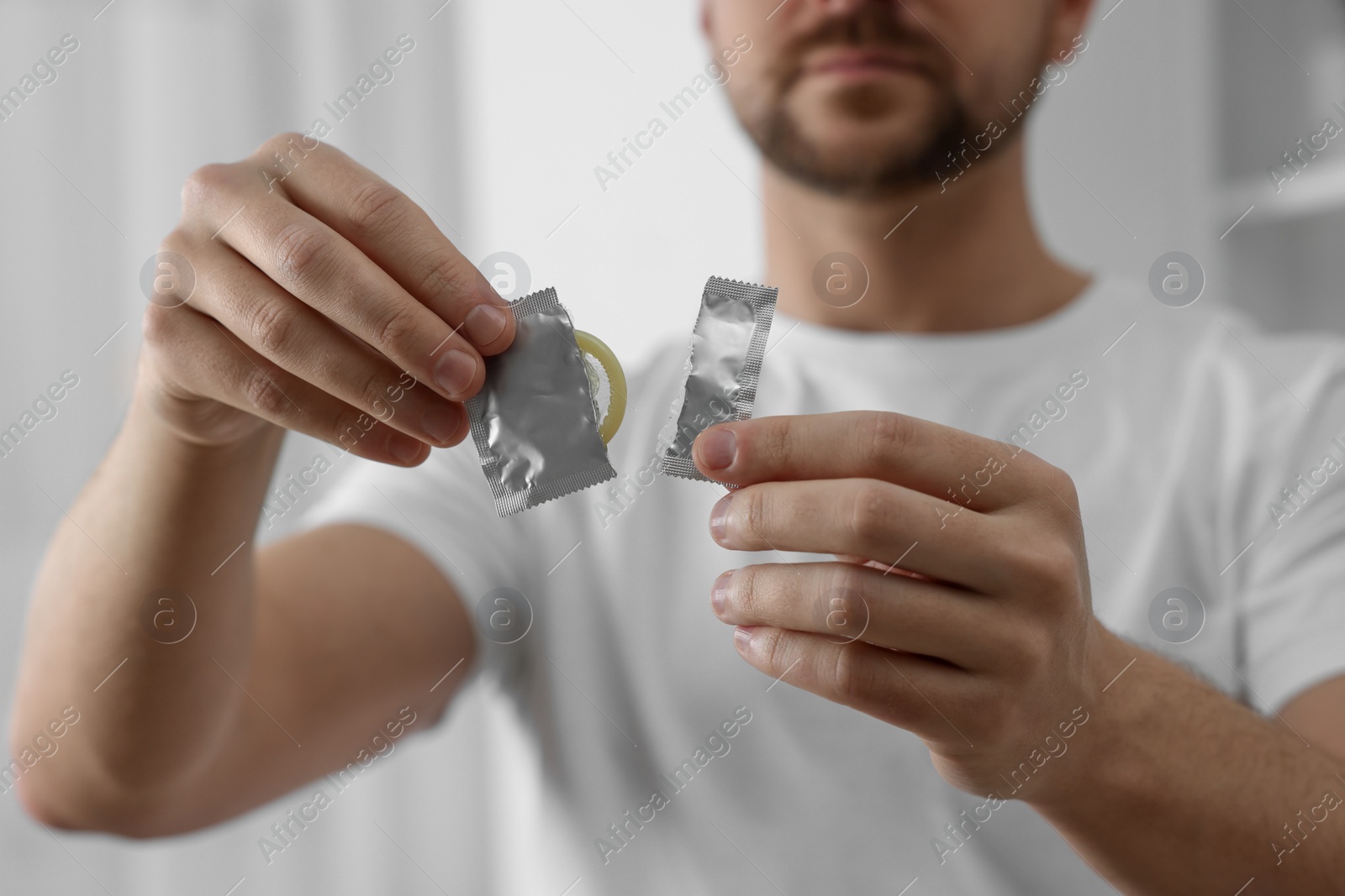 Photo of Closeup of man holding open pack with condom on blurred background