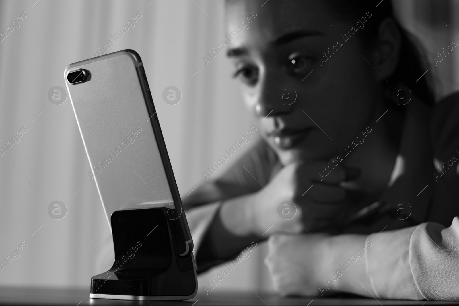 Photo of Lonely woman with mobile phone at table indoors, space for text. Black and white effect