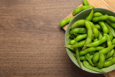 Photo of Bowl with green edamame beans in pods on wooden table, top view. Space for text
