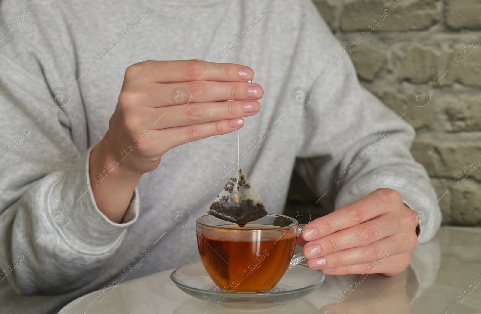 Photo of Woman taking tea bag out of cup at table indoors, closeup