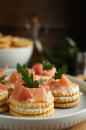 Photo of Delicious crackers with cream cheese, prosciutto and parsley on plate, closeup