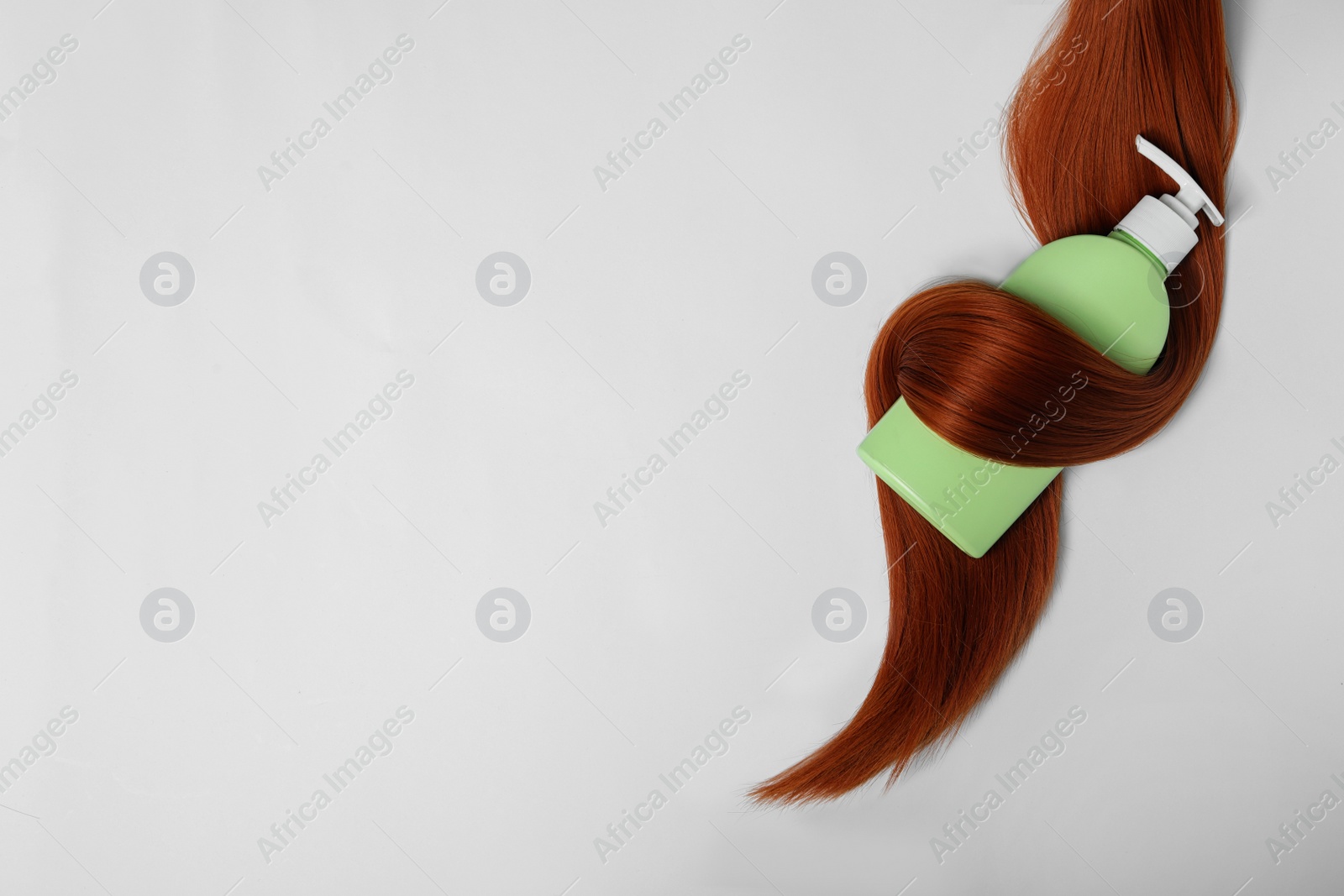 Photo of Shampoo bottle wrapped in lock of hair isolated on white, top view. Natural cosmetic products