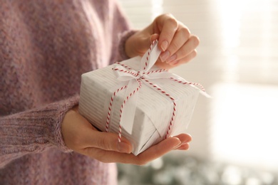 Woman holding white Christmas gift box indoors, closeup