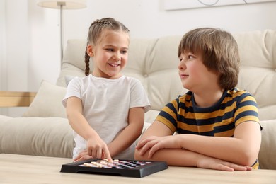 Photo of Cute boy playing checkers with little girl at light wooden table in room