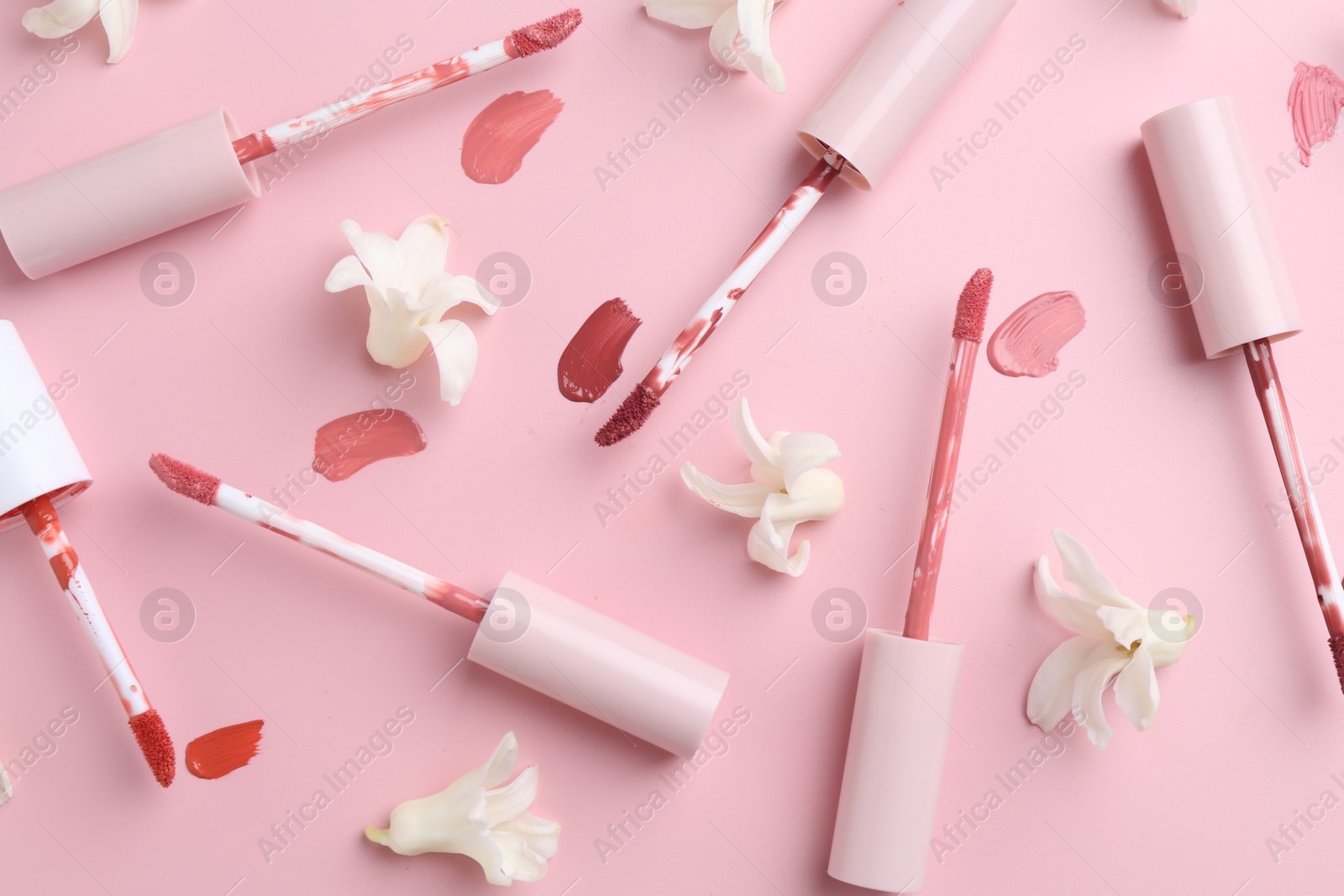 Photo of Different lip glosses, applicators and flowers on pink background, flat lay