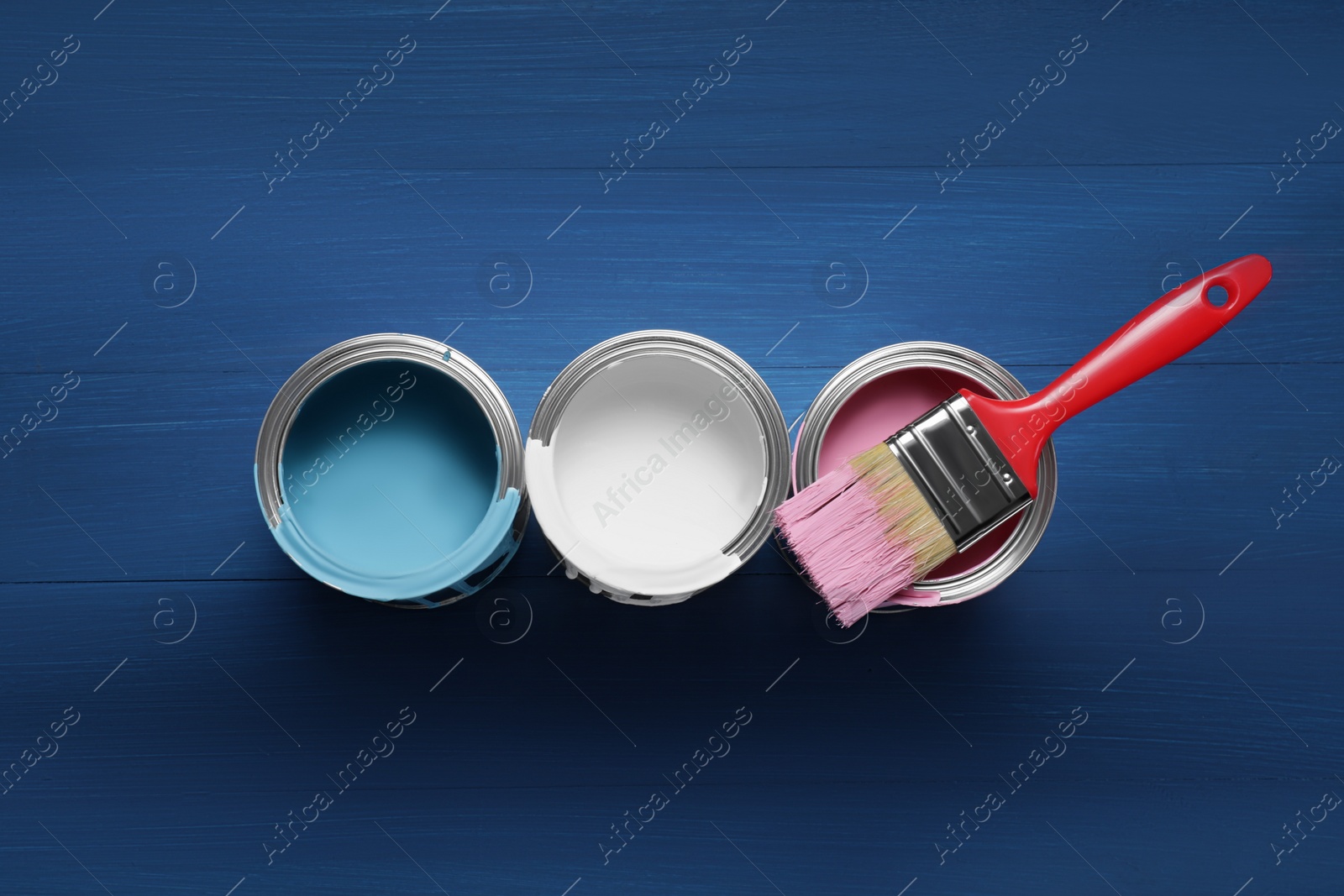 Photo of Cans of paints and brush on blue wooden background, flat lay