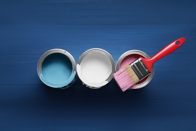 Photo of Cans of paints and brush on blue wooden background, flat lay