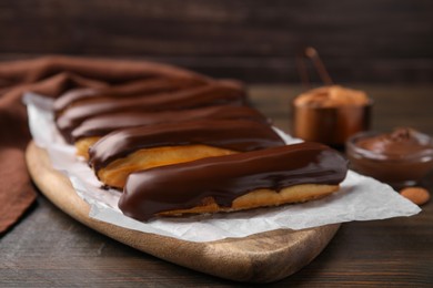 Photo of Delicious eclairs covered with chocolate on wooden table, closeup