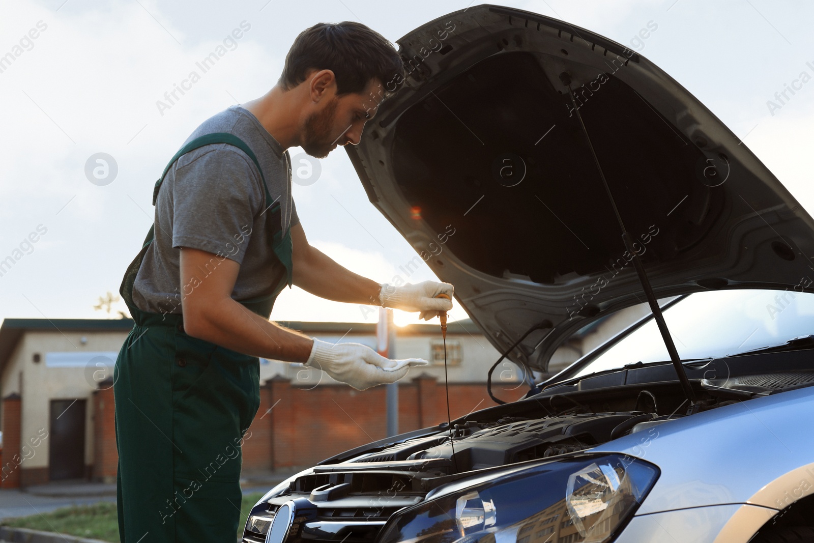 Photo of Worker checking motor oil level with dipstick outdoors