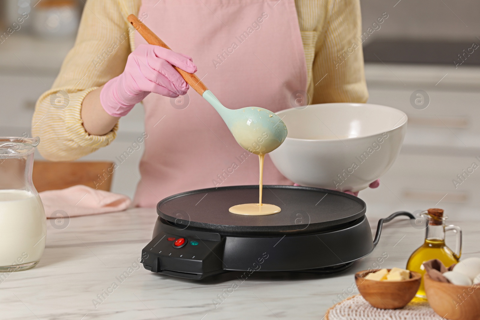 Photo of Woman cooking delicious crepe on electric pancake maker at white marble table in kitchen, closeup