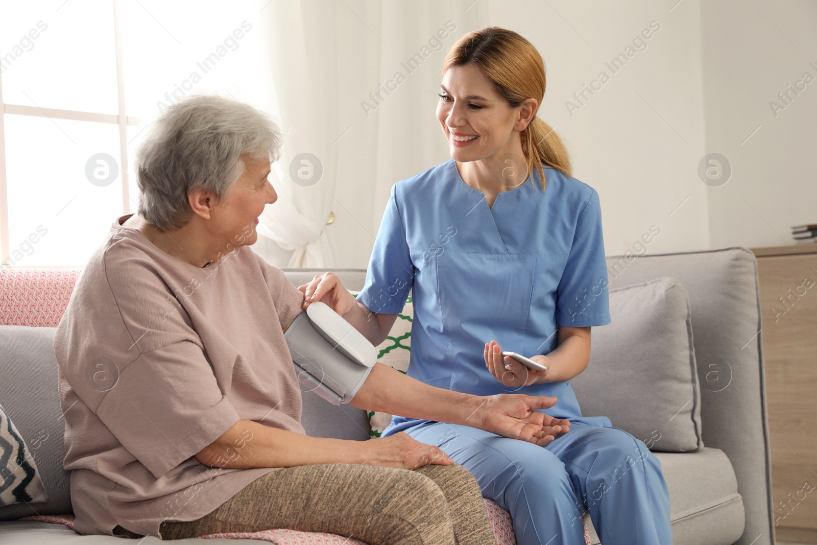 Photo of Nurse measuring blood pressure of elderly woman indoors. Assisting senior people