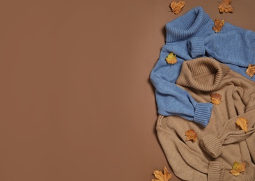 Photo of Warm sweaters and dry leaves on brown background, flat lay with space for text. Autumn season