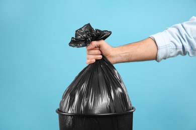 Photo of Woman taking garbage bag out of bin on light blue background, closeup