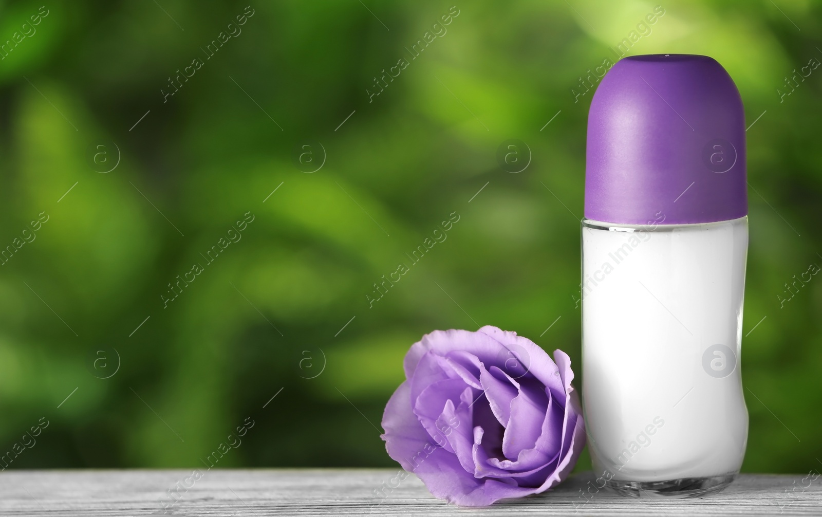 Photo of Natural deodorant with eustoma on wooden table against blurred green background. Space for text