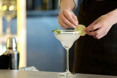 Woman preparing fresh alcoholic cocktail with lime and mint at bar counter, closeup view