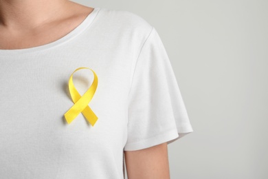 Photo of Woman with yellow ribbon on t-shirt against light background. Cancer awareness