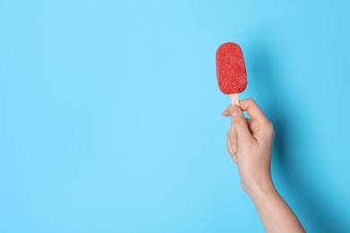 Woman holding tasty fruit ice pop on light blue background, space for text