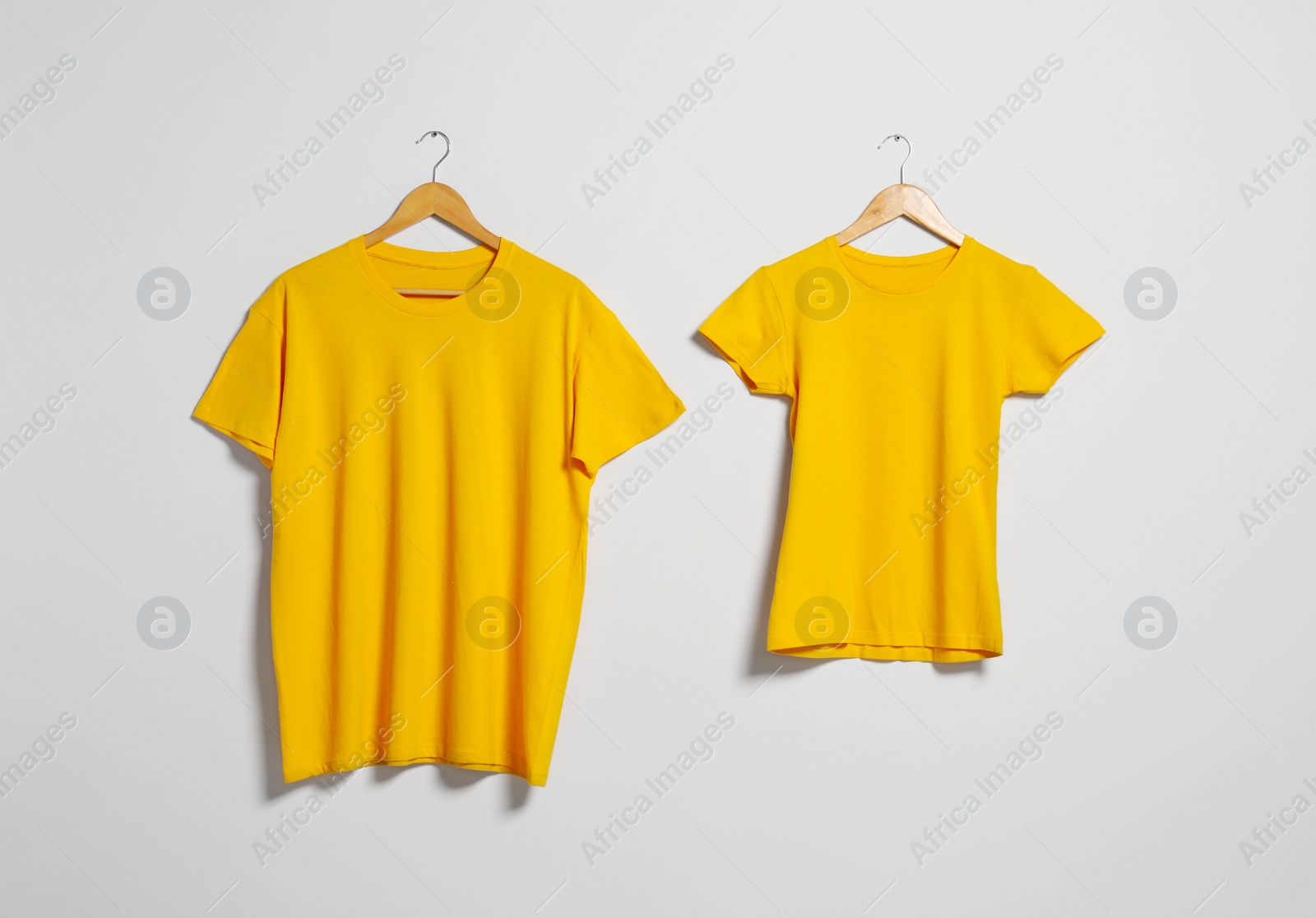 Photo of Hangers with different t-shirts on light wall. Mockup for design