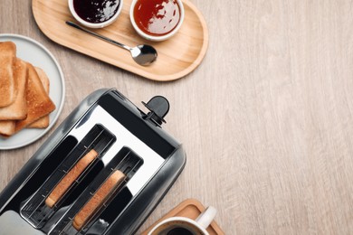 Toaster, roasted bread, jams and coffee on wooden table, flat lay. Space for text