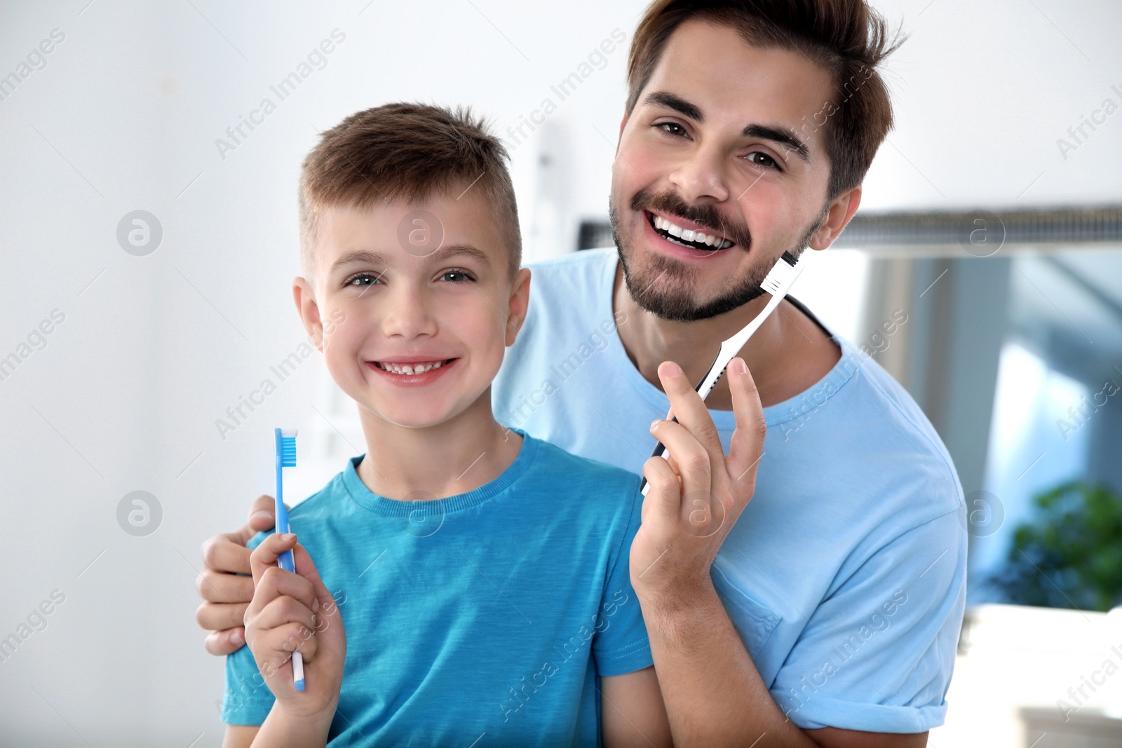 Photo of Portrait of young man and his son with toothbrushes in bathroom. Personal hygiene