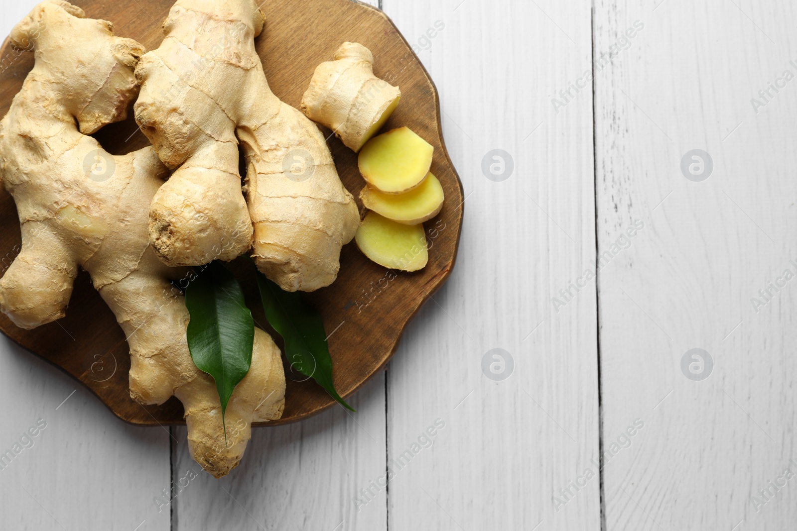 Photo of Fresh ginger with leaves on white wooden table, top view. Space for text