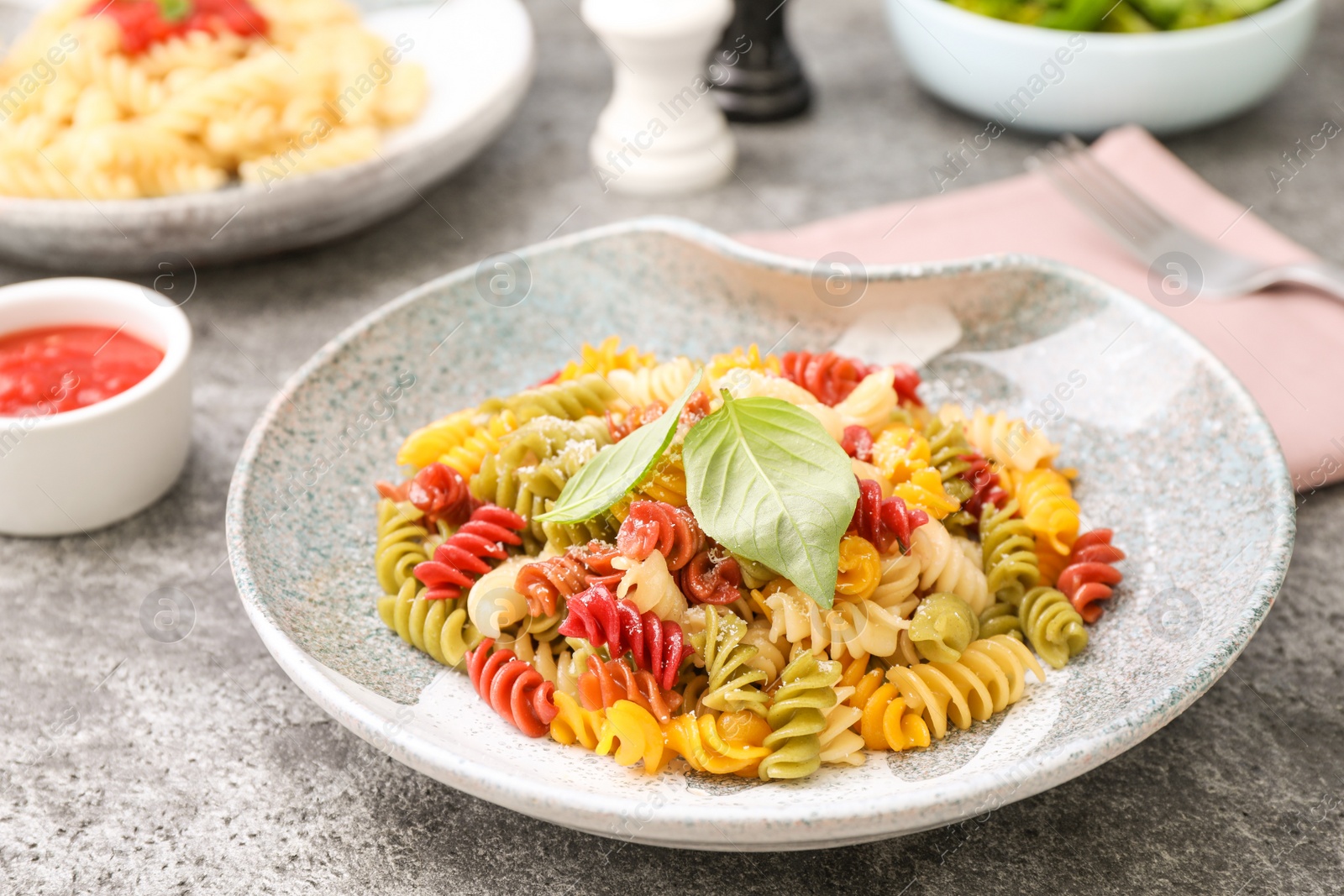 Photo of Colorful pasta with basil and cheese on grey table, closeup