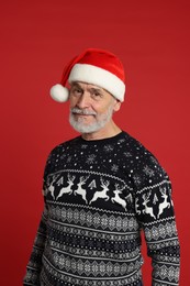 Photo of Senior man in Christmas sweater and Santa hat on red background